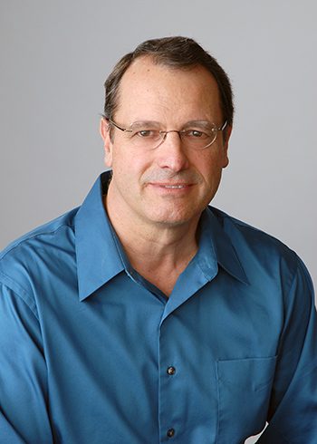 A man in blue shirt and glasses smiling for the camera.